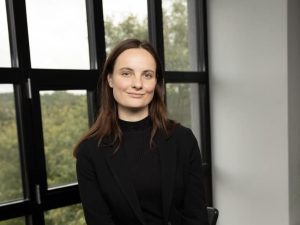 Emilija Švobaitė, a white woman with brown hair wearing a black jumper. She is sitting in front of a window.